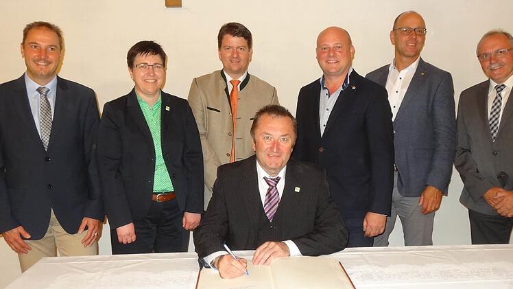 Udo Baumann (sitzend) trägt sich in das Goldene Buch der Stadt Bischofsheim im Beisein der Kreuzbergallianz-Bürgermeister ein (von links): stellvertretender Bürgermeister der Gemeinde Sandberg Roland Bühner, Bürgermeisterin Birigt Erb (Oberelsbach), Sandro Kirchner (MdL), Georg Seiffert (designierter Bürgermeister der Stadt Bischofsheim), Bürgermeister Gerd Kleinhenz (Wildflecken) und Bürgermeister Rudi Zehe (Schönau). Foto: Marion Eckert