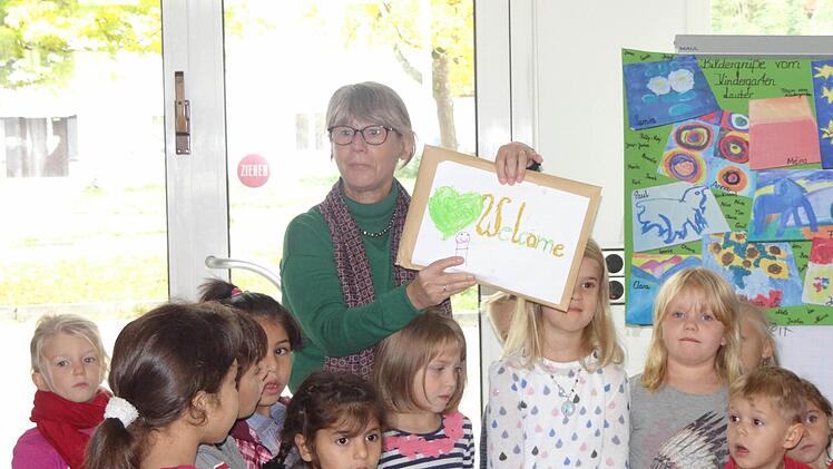 Miteinander, füreinander: Die Kinder aus Lauter haben zugunsten der Eberner Flüchtlingskinder Bilder nach Vorlagen großer Künstler gemalt (hinten rechts). Mit im Bild bei einem Besuch in der Flüchtlingsunterkunft in der alten Kaserne ist Kindergartenleiterin Anette Müller, die ein Willkommensschild hochhält. Foto: Johanna Eckert