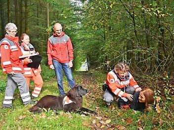 Die gefundene Person musste der Hund anzeigen und bei ihr bleiben, so wie hier der sechsjährige Aron, ein Hovawart, bis sein Frauchen, Brigitte Lutz von der Hundestaffel Hassfurt, vor Ort war und erste Hilfe leisten konnte. BRK Kreisgeschäftsführer Hubert Kießner ließ sich von der Begleit-Prüferin Michaela Hanika und Prüferin Maria Hoffmann die Situation erläutern.  Foto: Hanns Friedrich