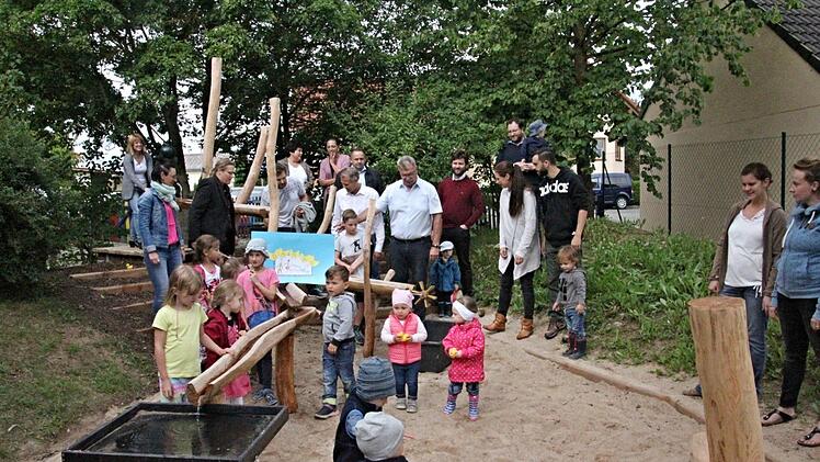 Wasser zieht Kinder magisch an. Das zeigte sich, als der Wasserspielplatz im Kindergarten Memmelsdorf eröffnet wurde. Auf dem Foto freuen sich mit den Kindern und Eltern Pfarrerin Sonja von Aschen (hinten 3. von links), sowie Bürgermeister Helmut Dietz und Firmenchef Stephan Rösler (Mitte, weiße Hemden von rechts). Foto: Helmut Will