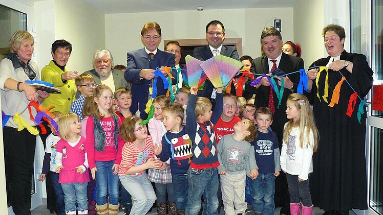 Im Beisein der Kinder wurde mit dem Durchschneiden eines bunt geschmückten Bandes die neue Rugendorfer Kinderkrippe freigegeben. Unser Bild zeigt umrahmt von den Kleinen der Gemeinde Rugendorf (von links) Leiterin Waltraud Bauer, MdL Inge Aures, Architekt Hans Spindler, Bürgermeister Martin Weiß, stellvertretender VG-Vorsitzenden Bernd Kotschenreuther (verdeckt), MdL Martin Schöffel, Landrat Klaus Peter Söllner und Pfarrerin Kathrin Klinger. Foto: Klaus-Peter Wulf