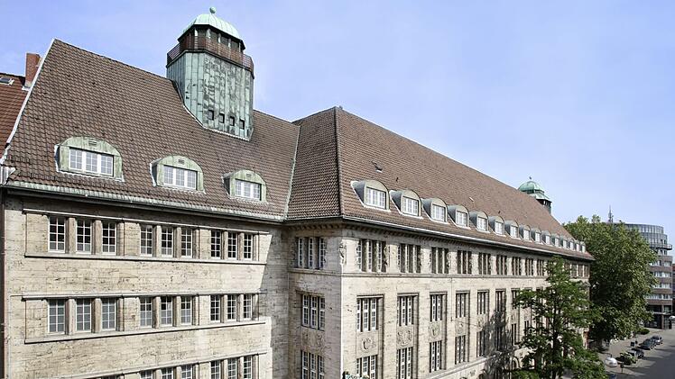 Historisches Gebäude mit steinernen Fassaden und charakteristischen Dächern. Es hat zahlreiche Fensterreihen und einen markanten Eingang. Eine bekannte Marke ist dort vertreten.