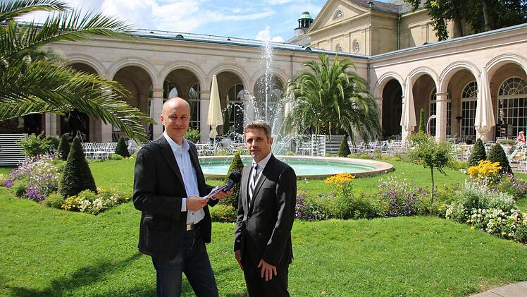 Interview-Termin in malerischer Atmosphäre: Redakteur Ralf Ruppert (von links) traf sich mit Kurdirektor Frank Oette im Kurgarten, im Hintergrund ein Teil des Arkedenbaus und der Regentenbau. Foto: Sebastian Elsässer