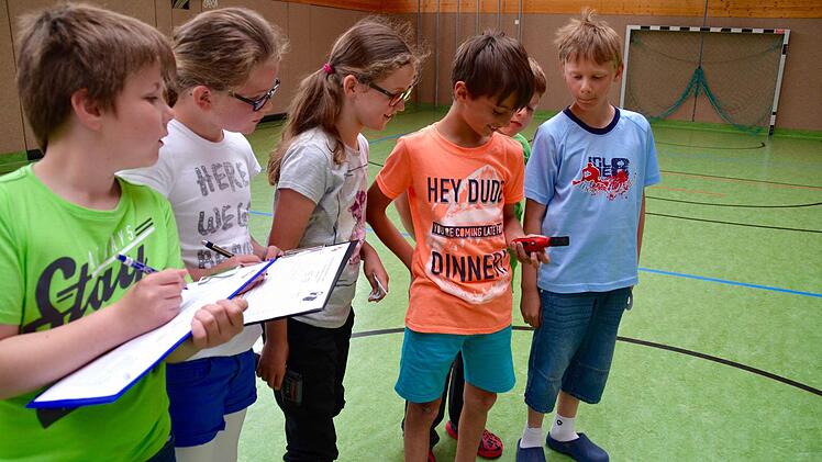 Die Energiedetektive sind in der Turnhalle der Grundschule Lauter unterwegs: Hier misst Xaver die Lichtintensität in der Halle. Während Kevin (von rechts), Linus und Lilia dabei genau zuschauen, tragen Sina und Marco die Messwerte in ihre Tabellen ein. Foto: Kathrin Kupka-Hahn