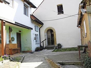 Zwischen beiden Türen hängt die Tafel an der Wand am oberen Eingang der Klaussteinkapelle. Man muss dazu um den Bauernhof herumgehen, der hier mit der Kirche verschmilzt. Foto: Reinhard Löwisch
