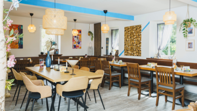 Helles, gem&uuml;tliches Restaurant mit modernen Holzm&ouml;beln und farbenfroher Deko. Gro&szlig;e Fenster lassen viel Licht hinein. Stilvolle Lampen und Pflanzen schaffen eine einladende Atmosph&auml;re.