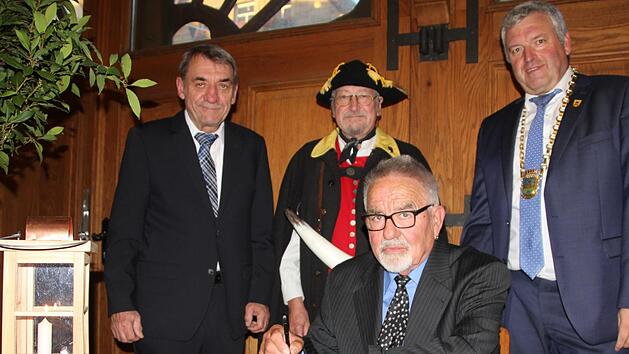 Ins Buch der Stadt trugen sich als neue Tr&auml;ger der B&uuml;rgermedaille Hans Elflein (sitzend) und Armin Dominka ein. Flankiert wurden sie vom Landrats-Stellvertreter Oskar Ebert (links) und B&uuml;rgermeister J&uuml;rgen Hennemann. Dominka wurden von Kollegen aus K&ouml;nigsberg und Bad Rodach begleitet. F&uuml;r den musikalischen Rahmen sorgte das Blasorchester Ebern&nbsp;Ralf Kestel