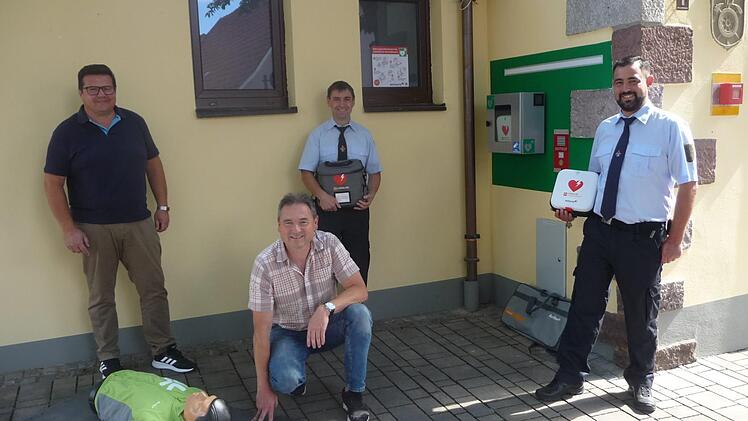 Peter Brunner (von links), Ortsbeauftragter Bernd Hüfner (kniend), Stellvertretender Kommandant Marko Koch und 1. Kommandant Dennis Frey bei der Vorstellung des neuen Defibrillators am Feuerwehrhaus.