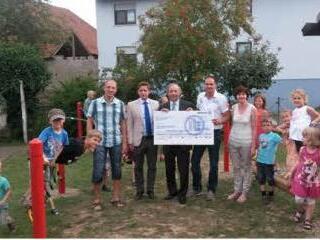 Vertreter der Allianz haben bei der Einweihung der Spielgeräte für die Kindertagesstätte Wasserlosen einen symbolischen Scheck überreicht. Auch andere regionale Firmen hatten das Projekt unterstützt.  Foto: Kita