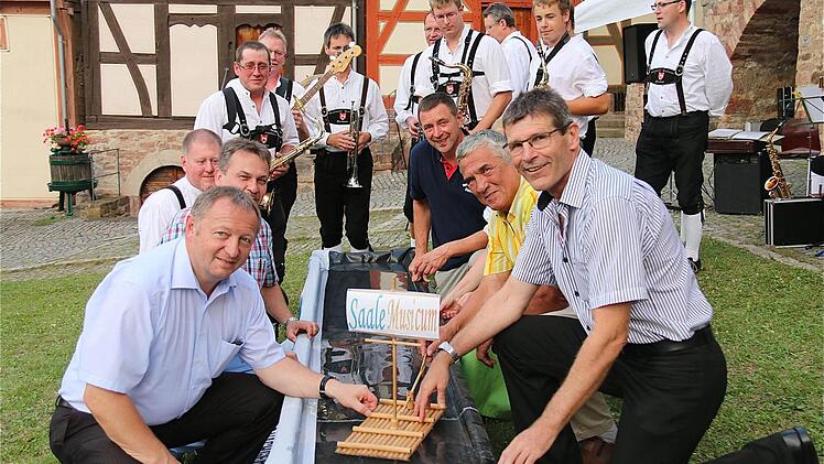 Die Floßübergabe (links von vorn): Thomas Bold, Kuno Holzheimer; (rechts von vorn): Thomas Schiebel, Alfred Frank und Peter Scherpf. Im Hintergrund die Klingenthaler Musikanten.
