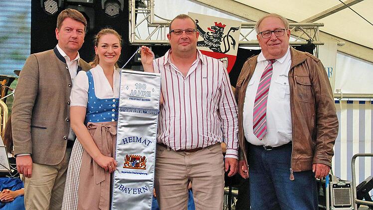 Einen überdimensionalen Wimpel "100 Jahre Freistaat Bayern" überreichten  Landtagsabgeordneter Sandro Kirchner (links) und Staatsministerin Judith  Gerlach dem Vorsitzenden des TSV Thundorf, Dieter Büchner (2. von rechts)  und dem Ehrenvorsitzenden Philipp Bauernschubert (rechts). Foto: Dieter  Britz