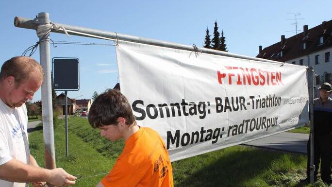 Steffen Kölbl, Jonas Bunzelt und Michael Schardt (v.l.) bringen einige Wochen vor dem Termin die Banner für die Radtourpur an.  Foto: Stefan Lutter