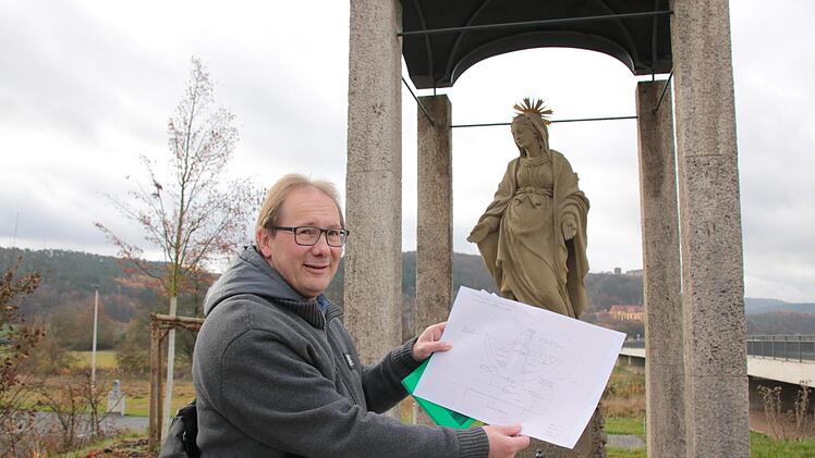 Stadtpfarrer Thomas Eschenbacher zeigt einen Plan der Schale mit Spatz darauf, die er vor der schwangeren Madonna an der neuen Saale-Brücke aufstellen lassen will. Foto: Ralf Ruppert
