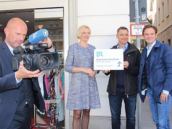 Norbert Küber, stellvertretender Leiter des Studios Franken filmt, Kathrin Degmaier, Leiterin des Studios Franken in Nürnberg und die Reporter Markus Klingele und Christian Limpert halten das neue Hinweisschild (von links). Foto: Simone Bastian