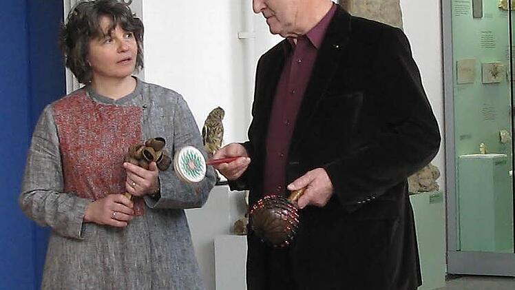 Die Rasseln, die Jürgen Werobèl-La Rochelle hier Kuratorin Astrid Weschenfelder vorführt, hat er aus Afrika mitgebracht. Die Musikinstrumente sind aus Nusschalen gefertigt. Foto: Daniela Pondelicek