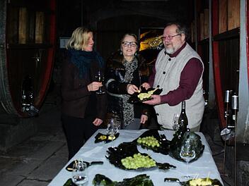 An der mit Weinflaschenkunst dekorierten Tafel erklärt Petra Markert (links) im Hammelburger Holzfasskeller den Kunstvereint-Mitgliedern Maria Rinecker und Rainer Stein Details ihres Schaffens. Winfried Ehling
