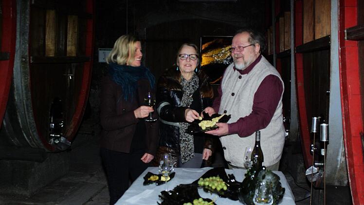 An der mit Weinflaschenkunst dekorierten Tafel erklärt Petra Markert (links) im Hammelburger Holzfasskeller den Kunstvereint-Mitgliedern Maria Rinecker und Rainer Stein Details ihres Schaffens. Winfried Ehling