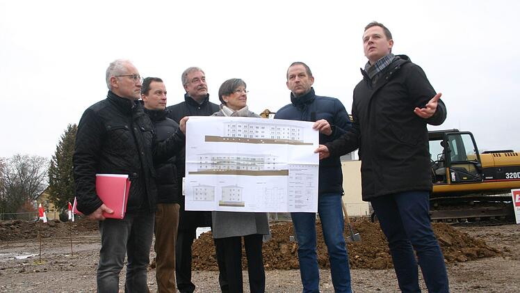Einen Blick darauf, wie das jetzt leere Gel&auml;nde in der Max-Roesler-Stra&szlig;e im Herbst 2020 aussehen soll, warfen K&auml;mmerer Michael Fischer, Architekt Martin G&ouml;hring,   Gesch&auml;ftsf&uuml;hrer Rainer Mayerbacher (Wohnungsbaugesellschaft), Regierungspr&auml;sidentin  Heidrun Piwernetz,  stellvertretender Landrat Rainer Mattern und B&uuml;rgermeister Tobias Ehrlicher (von links). Foto: Martin Rebhan