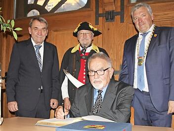 Ins Buch der Stadt trugen sich als neue Träger der Bürgermedaille Hans Elflein (sitzend) und Armin Dominka ein. Flankiert wurden sie vom Landrats-Stellvertreter Oskar Ebert (links) und Bürgermeister Jürgen Hennemann. Dominka wurde von Kollegen aus Königsberg und Bad Rodach begleitet. Für den musikalischen Rahmen sorgte das Blasorchester Ebern.  Foto: Ralf Kestel