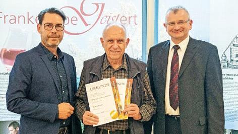 Mathias Kr&ouml;ner, Brennereifachberater der LWG Veitsh&ouml;chheim (l.), und Hubert Fr&ouml;hlich, der Vorsitzende des Kleinbrennerverbands (r.), &uuml;berreichten Herbert Lawrenz die Urkunden. Foto: privat