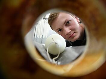 Wachszieher-Azubi André Ihl von der Firma Richard Wenzel in Aschaffenburg blickt durch eine Maschine, mit der Kerzen gerade gezogen werden. Foto:  Ronald Rinklef