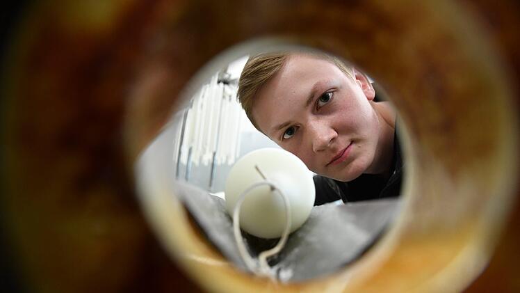 Wachszieher-Azubi André Ihl von der Firma Richard Wenzel in Aschaffenburg blickt durch eine Maschine, mit der Kerzen gerade gezogen werden. Foto:  Ronald Rinklef