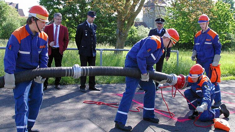 Kuppeln von vier Saugschläuchen lautet die erste Übung auf Zeit, die hier Jonas Hütter, Valentin Hopf, Jakob Buchmann und Mike Morgenroth absolvieren, beobachtet von Landrat Michael Busch (links) und Kreisbrandmeister Karl Ludwig Schmidt (rechts) als Wertungsrichter. Foto: Bettina Knauth