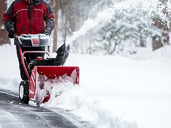 Eine Person, die eine Schneefr&auml;se bedient, um eine Auffahrt zu r&auml;umen. A person operating a snow blower to clear a driveway after a winter storm