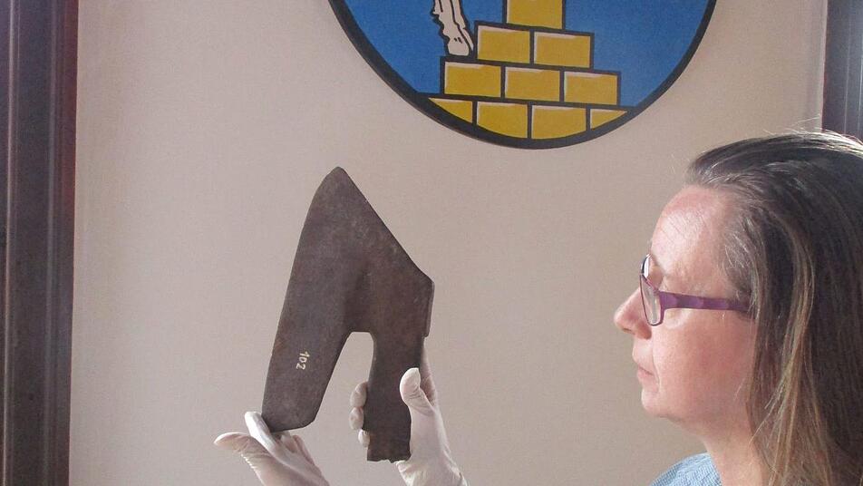 Stadtarchivarin Adelheid Waschka mit dem angeblichen "Henkersbeil" aus dem Depot des Stadtmuseums Bad Staffelstein. Der "kopflose Reiter" auf dem Wappen im Hintergrund entstand zufällig durch den gewählten Bildausschnitt und erscheint doch irgendwie passend. Der Einsatz eines solchen Beils für Hinrichtungen ist historisch allerdings nicht gesichert.  Foto: Andrea Zimmermann