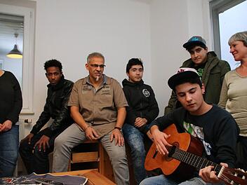 Der 17-jährige Hamodi spielt im Wohnzimmer Gitarre, Eki Stelzer, Samiel, Hassan Bel Mahdi, Rodi und Maria Herleth hören zu. Foto: Heike Beudert