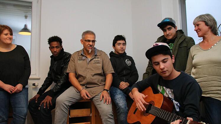 Der 17-jährige Hamodi spielt im Wohnzimmer Gitarre, Eki Stelzer, Samiel, Hassan Bel Mahdi, Rodi und Maria Herleth hören zu. Foto: Heike Beudert