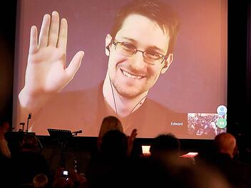 Der NSA-Enthüller Edward Snowden winkt am 14.12.2014 in Berlin während einer Videoschalte dem Publikum zu. Foto: Wolfgang Kumm/dpa