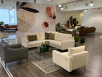 Ein weißes Sofa und zwei graue Stühle vor einer mit Blumen bemalten Trennwand im Showroom von W. Schillig.