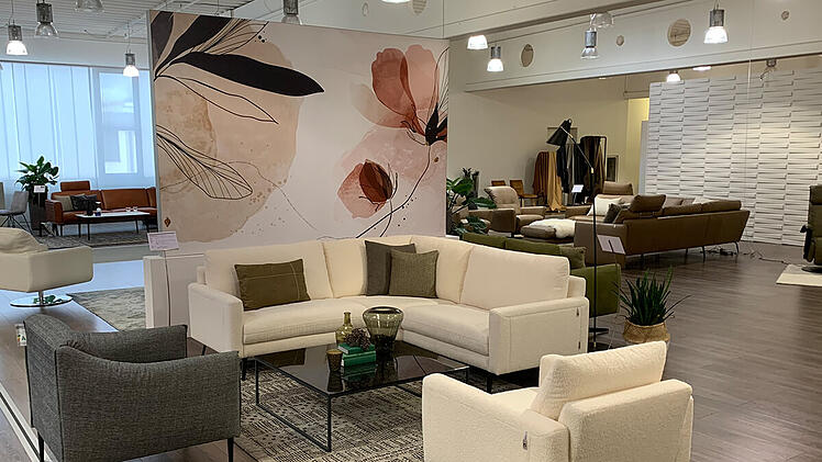 Ein weißes Sofa und zwei graue Stühle vor einer mit Blumen bemalten Trennwand im Showroom von W. Schillig.