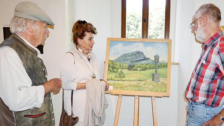 Herbert Schneider (rechts) zeigt derzeit 35 Bilder aus verschiedenen Epochen seiner Schaffensphasen im Bruder-Franz-Haus auf dem Kreuzberg. Gert Raimann und seine Frau Irene lassen sich vom Haselbacher Rhönmaler die Werke erläutern.  Foto: Marion Eckert