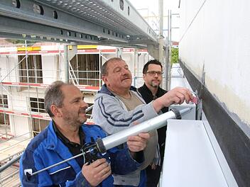 Nysret Imrihari (von links) und Reiner Stühler von der Firma "Haga" dichten nach dem Einbau der mehr als 200 Fenster die Fassade des Landratsamtes ab. Architekt Stephan Scharf betreut die Arbeiten. Im Hintergrund der Rohbau des Erweiterungsbaus. Foto: Ralf Ruppert