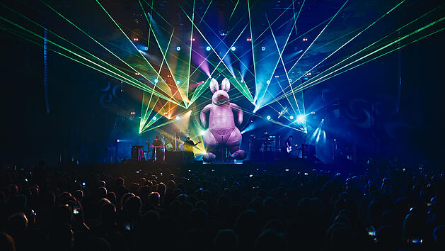 Lichtshow mit einer riesigen aufblasbaren Figur im Mittelpunkt, umgeben von bunten Laserstrahlen und einer Menschenmenge bei einem Konzert der Australian Pink Floyd Show.