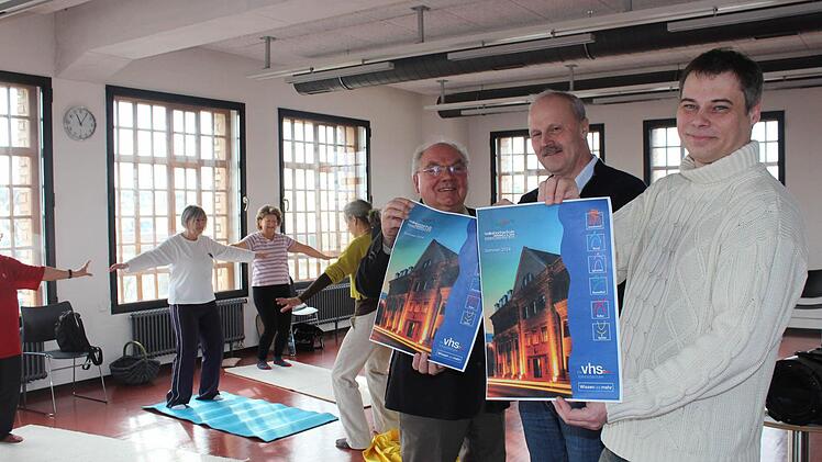 Während die Damen im Hintergrund sich bei Qi Gong entspannen, weisen (von links) Sebastian Schmidt, Bürgermeister Gerald Brehm und Thomas Reimer auf das neue Programmheft hin. Foto: Maria Leicht