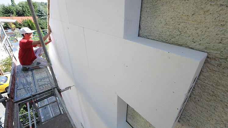 Ein Arbeiter befestigt eine Styroporplatte zur Wärmedämmung an einer Hausfassade in Straubing. Foto: Armin Weigel/dpa