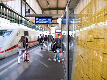 Ein Fahrplan hängt am Stuttgarter Hauptbahnhof. Im Hintergrund gehen Reisende zu einem ICE. Bahnkunden zwischen Berlin und Hamburg bekommen von Sonntag an einen kleinen Vorgeschmack auf den angestrebten bundesweiten Taktfahrplan. Foto: Tom Weller, dpa