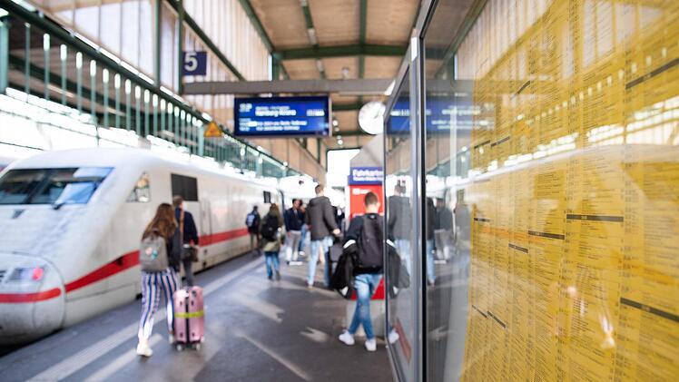 Ein Fahrplan hängt am Stuttgarter Hauptbahnhof. Im Hintergrund gehen Reisende zu einem ICE. Bahnkunden zwischen Berlin und Hamburg bekommen von Sonntag an einen kleinen Vorgeschmack auf den angestrebten bundesweiten Taktfahrplan. Foto: Tom Weller, dpa