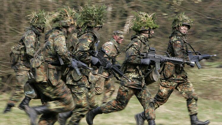Mit Blattwerk und Gras getarnte Wehrpflichtige von den Panzergrenadieren rennen mit ihren Waffen im Rahmen ihrer Grundausbildung bei einer Übung über das freie Gelände der Knüll Kaserne in Schwarzenborn. Die Union debattiert über «allgemeine Dienstpflicht» und Wehrpflicht. Foto: Frank May/dpa