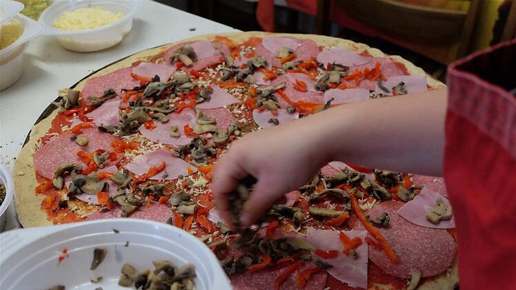 Fleißige Frauenhände streichen die eingedickte Tomatensoße über den Pizzarohling und belegen die Teiglinge mit leckeren Zutaten. Foto: Gerd Schaar