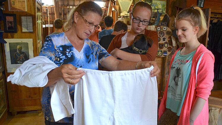 Lydia Muth zeigt Maja und Selina eine alte Unterhose. Über dem Arm hat sie das dazugehörige Unterhemd gelegt. Darin befindet sich noch ein Namensschild, bei dem es sich aber um kein Modelabel handelt. Im Hintergrund bestaunen die Jungs Handwerkliches. Foto: Kathrin Kupka-Hahn