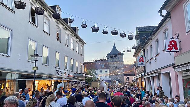 Menschenmenge auf dem Lichtenfelser Korbmarkt; Straßendekoration mit Körben, historische Architektur im Hintergrund, lebhafte Atmosphäre bei Abenddämmerung.