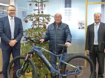Vorstandsvorsitzender Wolfgang Menninger (links) und Kassierer Ludwig Brumm (rechts) bei der Übergabe des E-Bikes an den Gewinner Lorenz Oppelt.
