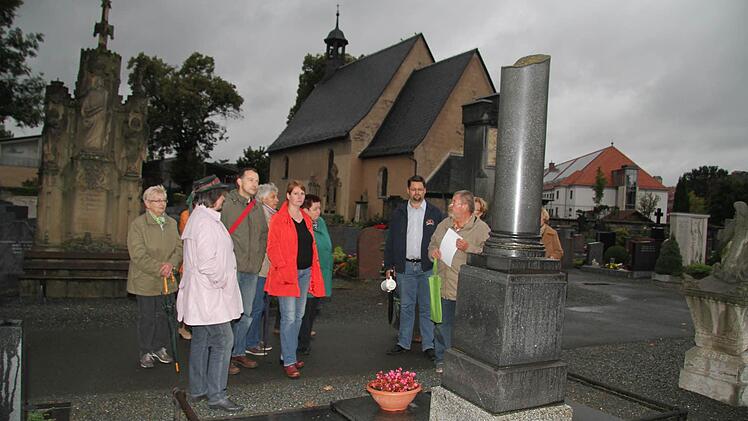 Manchmal weisen die Grabmäler auch auf die Personen, die an Ort und Stelle begraben sind, hin: Das Grab des Bezirksgeometers jedenfalls ist sehr schlicht gehalten - im Hintergrund das sehenswerte Grab der Familie Zimmermann und die Nikolauskapelle.