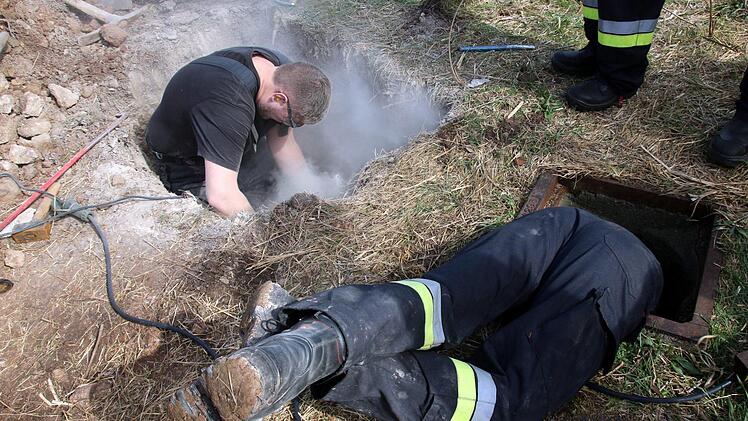 Während sich ein Feuerwehrmann links nach und nach durch die Betonplatte arbeitet, kontrolliert ein Kollege rechts, wie die Lage angesichts von Staub und Lärm unten im Kanal für den Hund aussieht.