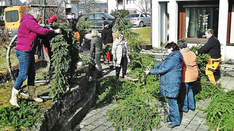 W&auml;hrend Edith Hahn (links) und die "Montagsbastler" bereits flei&szlig;ig am Binden sind, liefern Mitarbeiter des Bauhofs gro&szlig;e Mengen Fichtenzweige an. Mit rund 300 bunten Eiern beh&auml;ngt, wird die Osterkrone in den kommenden Wochen den Vorplatz des Friedrich-Baur-Seniorenzentrums Sankt Kunigund schm&uuml;cken.  Foto: Bernd Kleinert