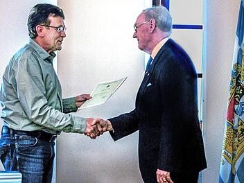 Die bayerische Fahne macht's feierlich: Josef Fuchs (links), im Landratsamt Haßberge für Einbürgerungen zuständig, übergibt die Einbürgerungsurkunde an Alan Stockbridge aus Ebern. Fotos: privat